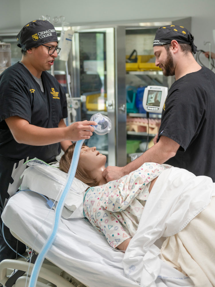 Nurse placing an oxygen mask on a patient in a hospital bed as another clinician holds the patient’s hand.
